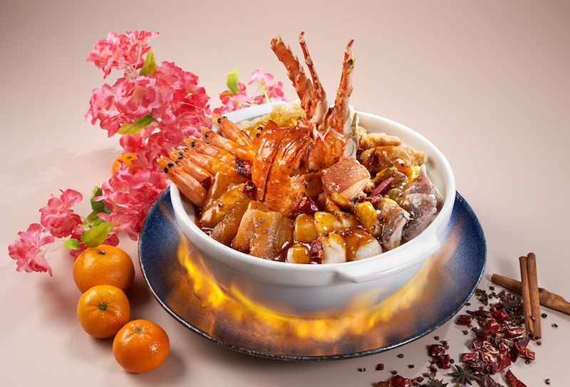 A claypot of pen cai with Chinese new year decorations by the side