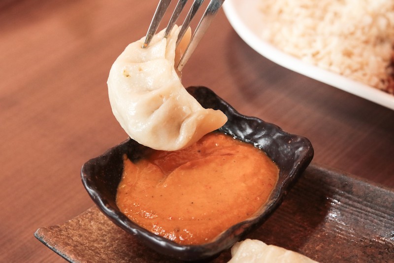 A chicken momo dipped in chilli sauce