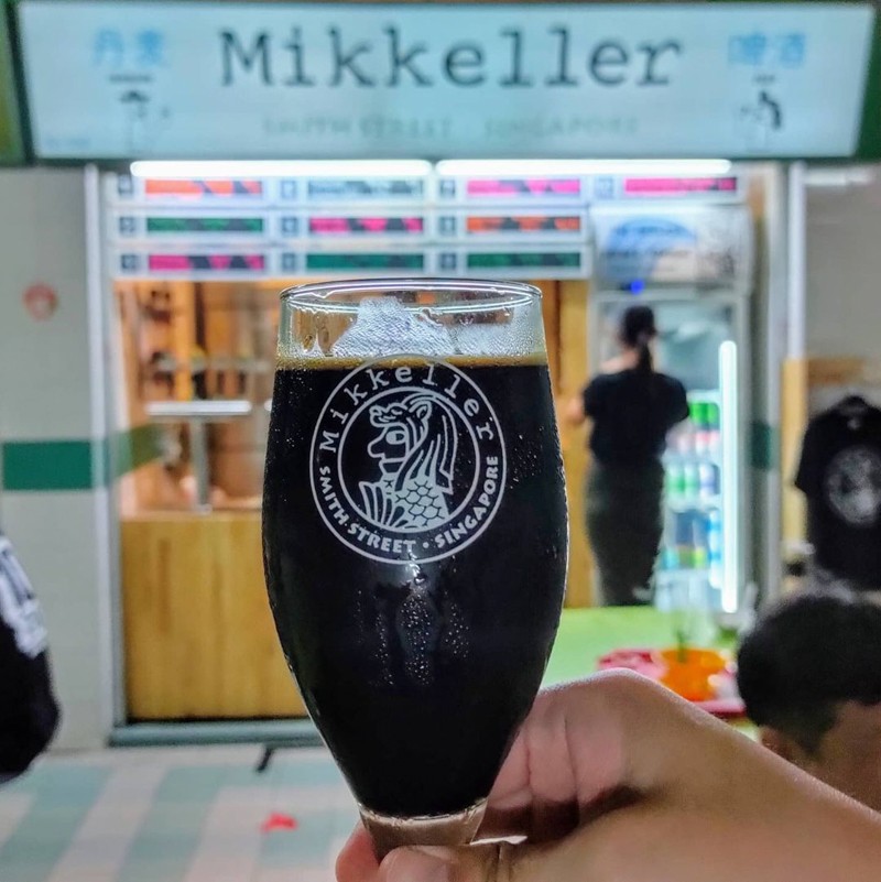 A glass of stout in front of Mikkeller Singapore 3