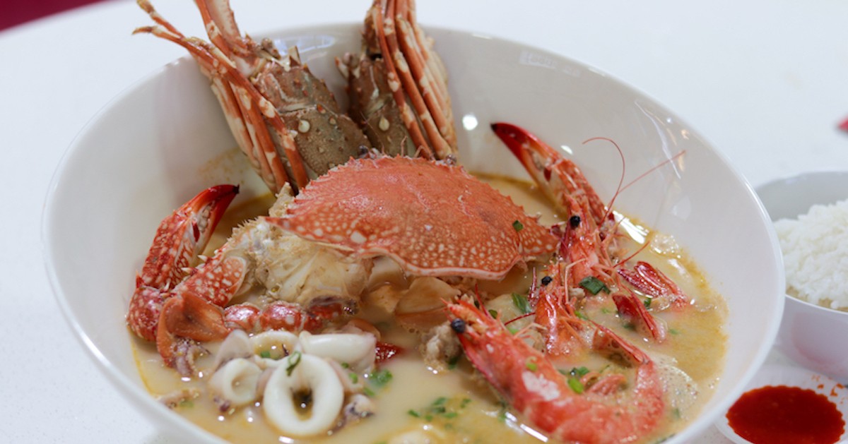 A bowl of XXL Seafood soup alongside saucers of chilli and a bowl of rice