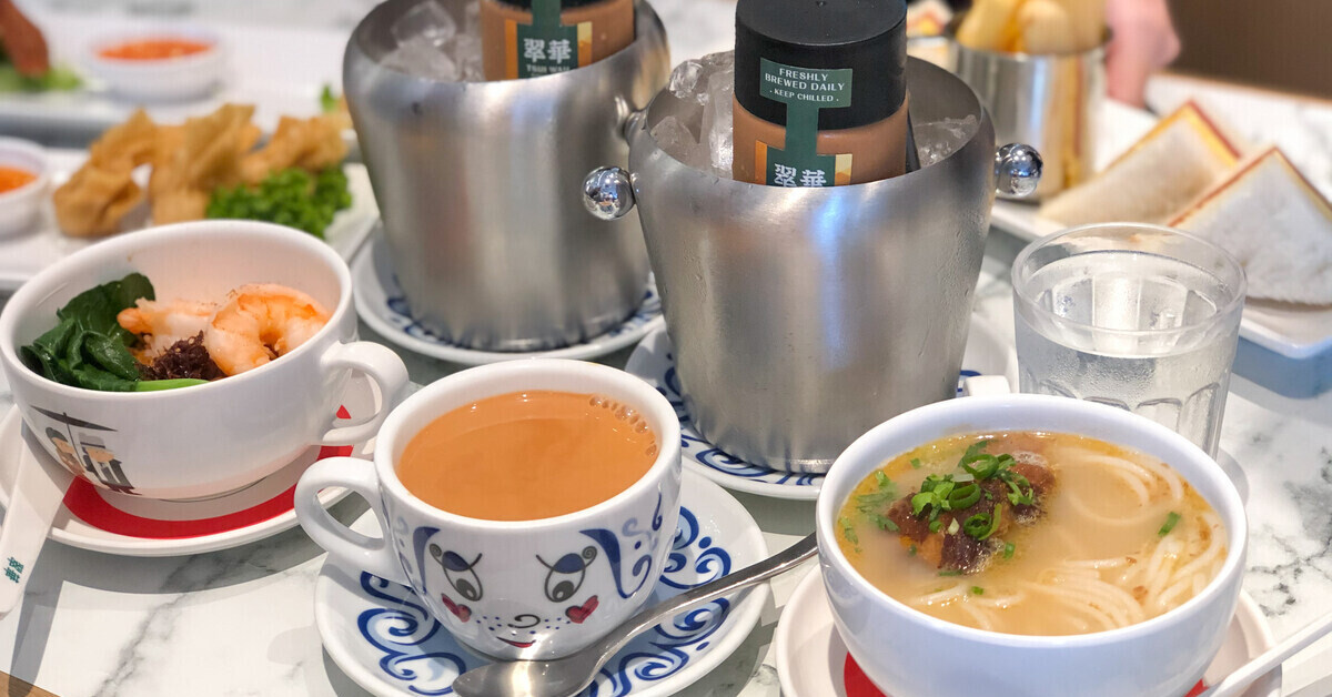 A spread of offerings at Tsui Wah's afternoon tea, including a cup of milk tea, noodle bowls, and bottled milk tea in a bucket