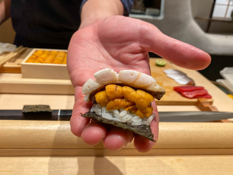 Hand holding roll of uni and tachiuo