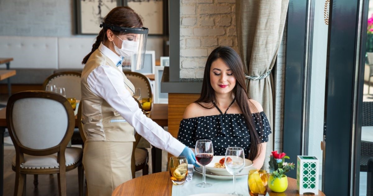 woman being served by waitress with mask