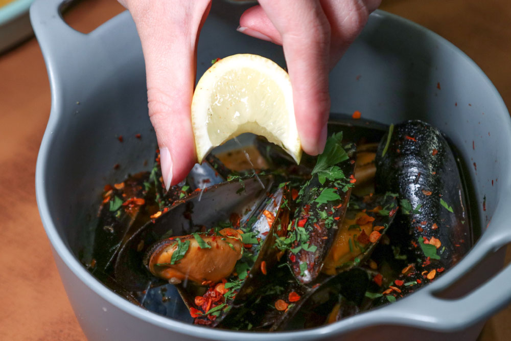 hand squeezing lemon over mussels