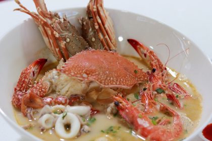 A bowl of XXL Seafood soup alongside saucers of chilli and a bowl of rice